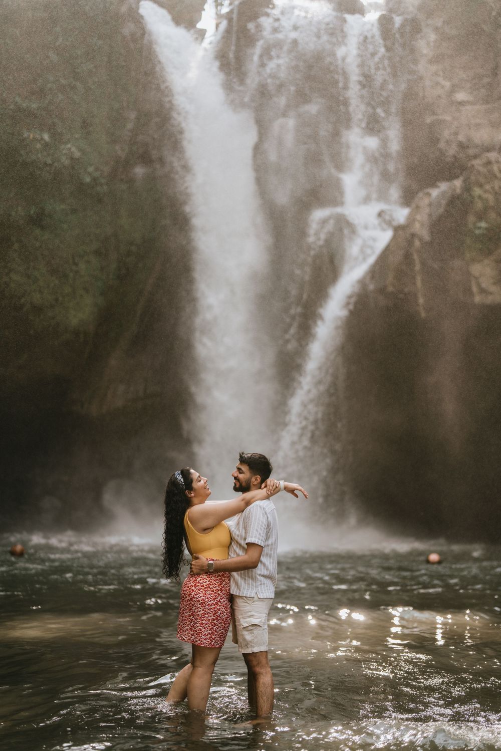 A couple wades in the pool beneath a magnificent waterfall during a romantic photoshoot.