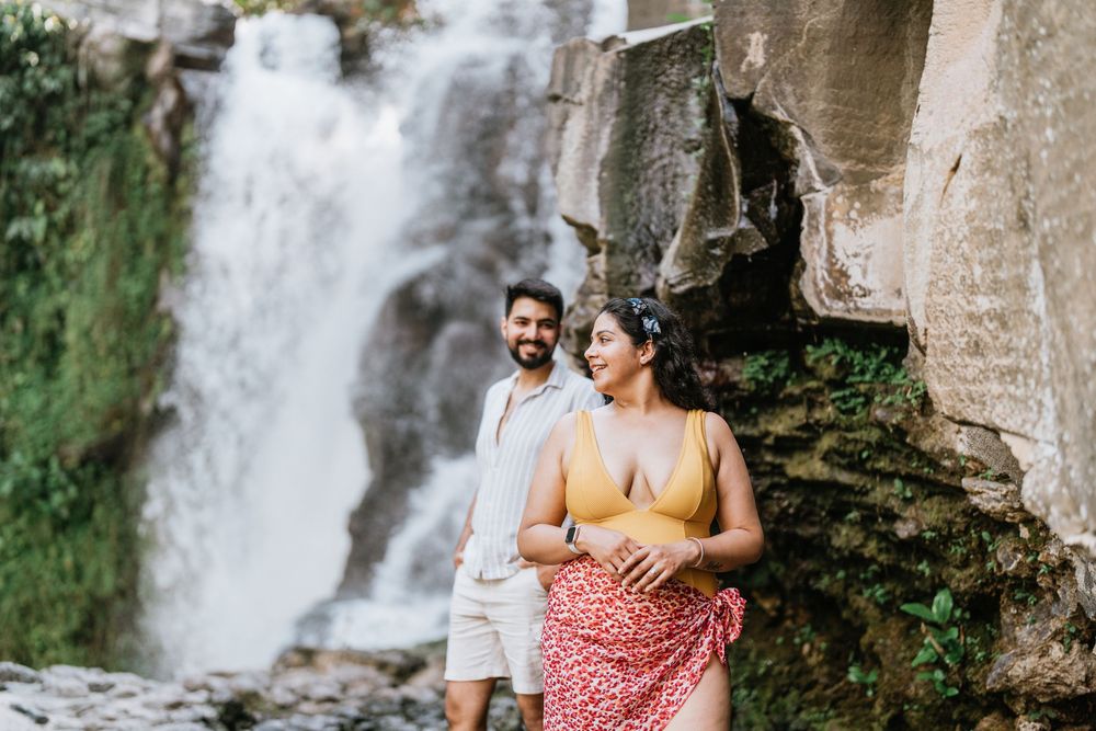 Couple posing together near a scenic waterfall with lush greenery.