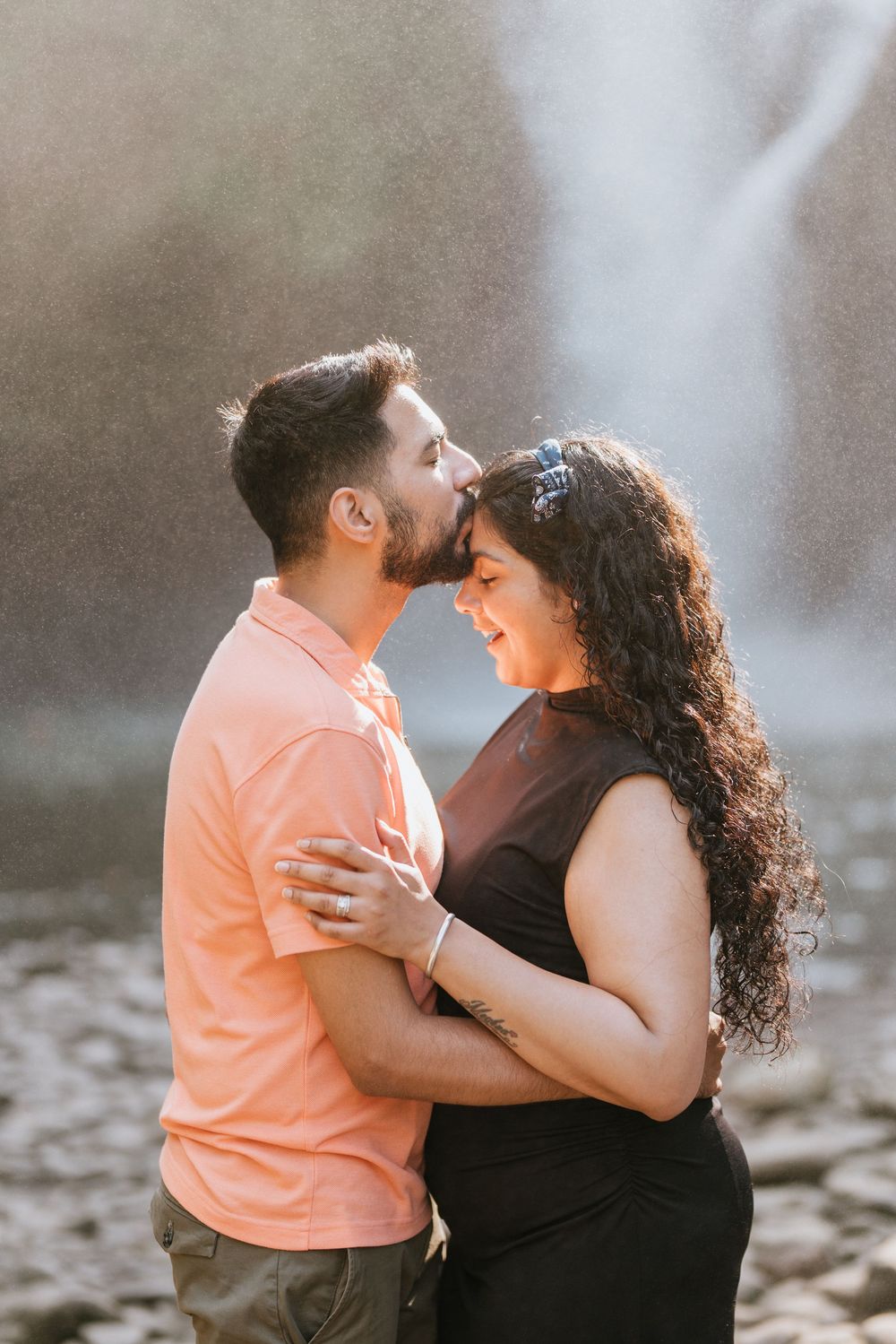 Couple embracing outdoors in warm sunlight with one wearing a peach colored shirt.