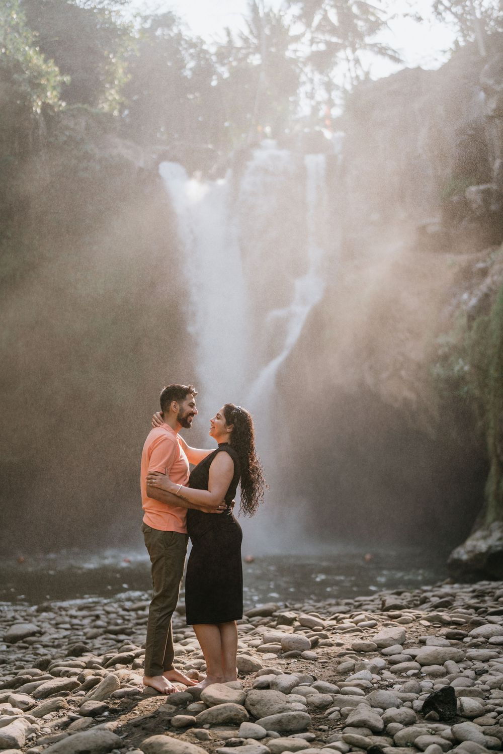 Romantic photoshoot by waterfall with sunbeams streaming through mist.