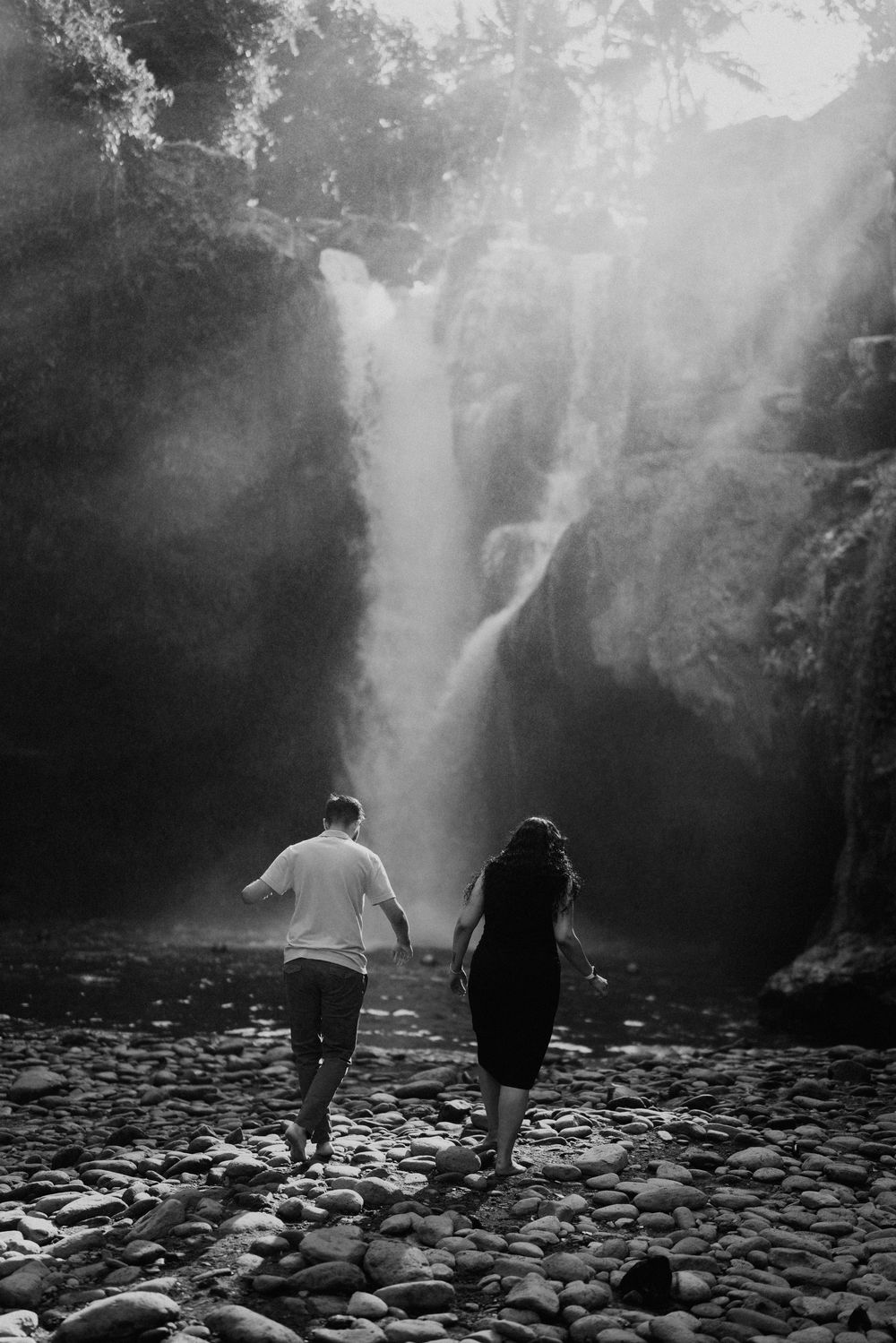 Silhouetted figures walking on rocky terrain towards a misty waterfall.