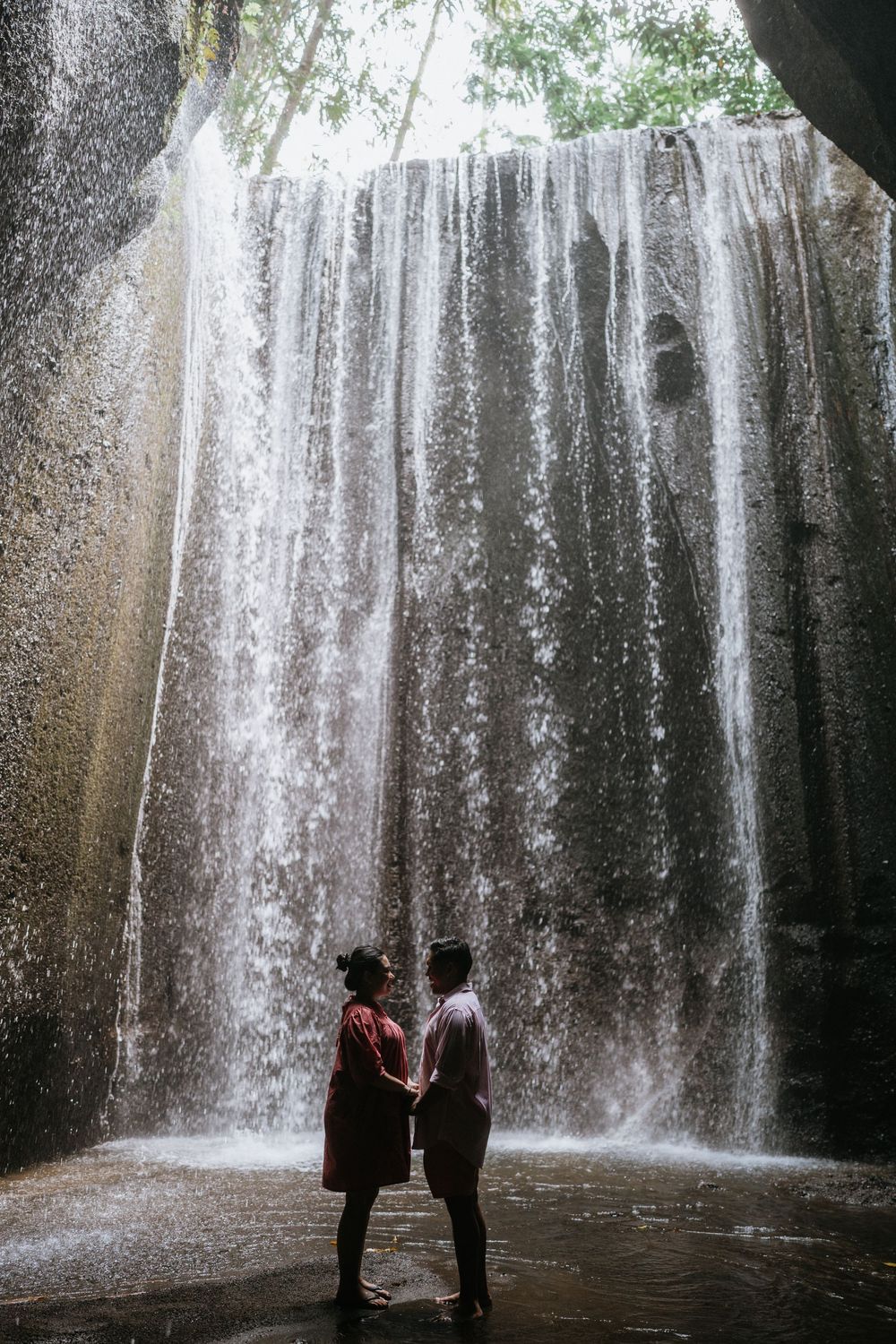 Silhouettes of two people standing before a cascading waterfall in a dark cave.
