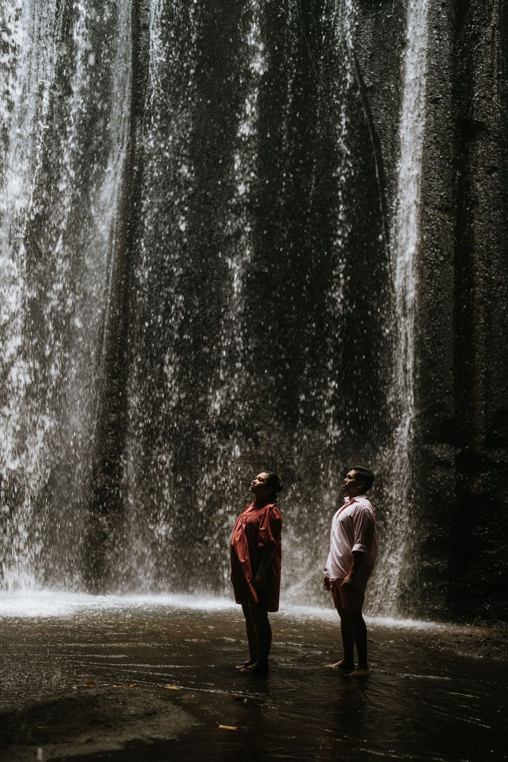 Two figures standing in conversation against a dramatic waterfall backdrop.