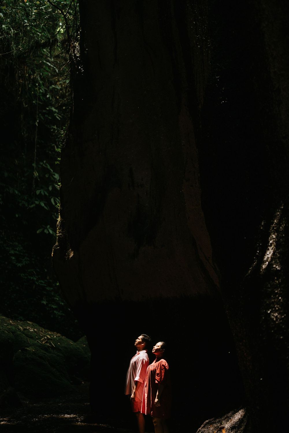 Two people in contrasting outfits walking through a shadowy forest path.