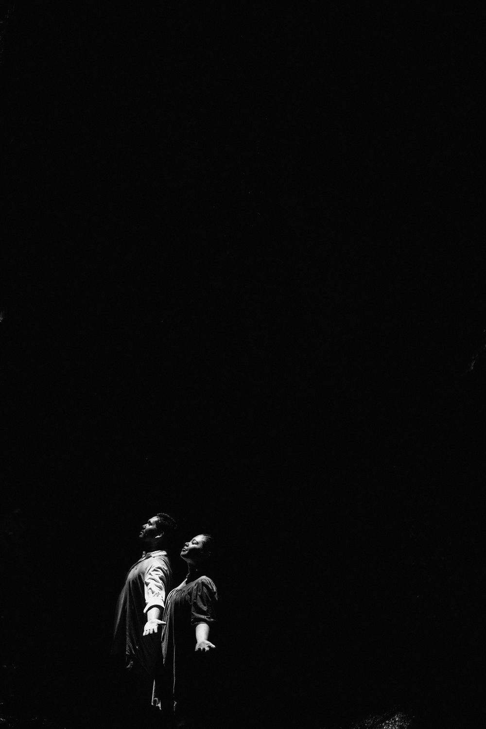 Artistic black and white photo of two people in an intimate pose against dark background.