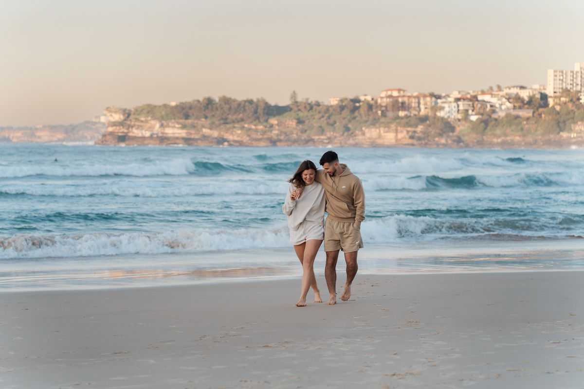 A couple walking hand in hand along a scenic Bondi beach at sunrise with waves rolling onto the shore during a couples photoshoot in Sydney