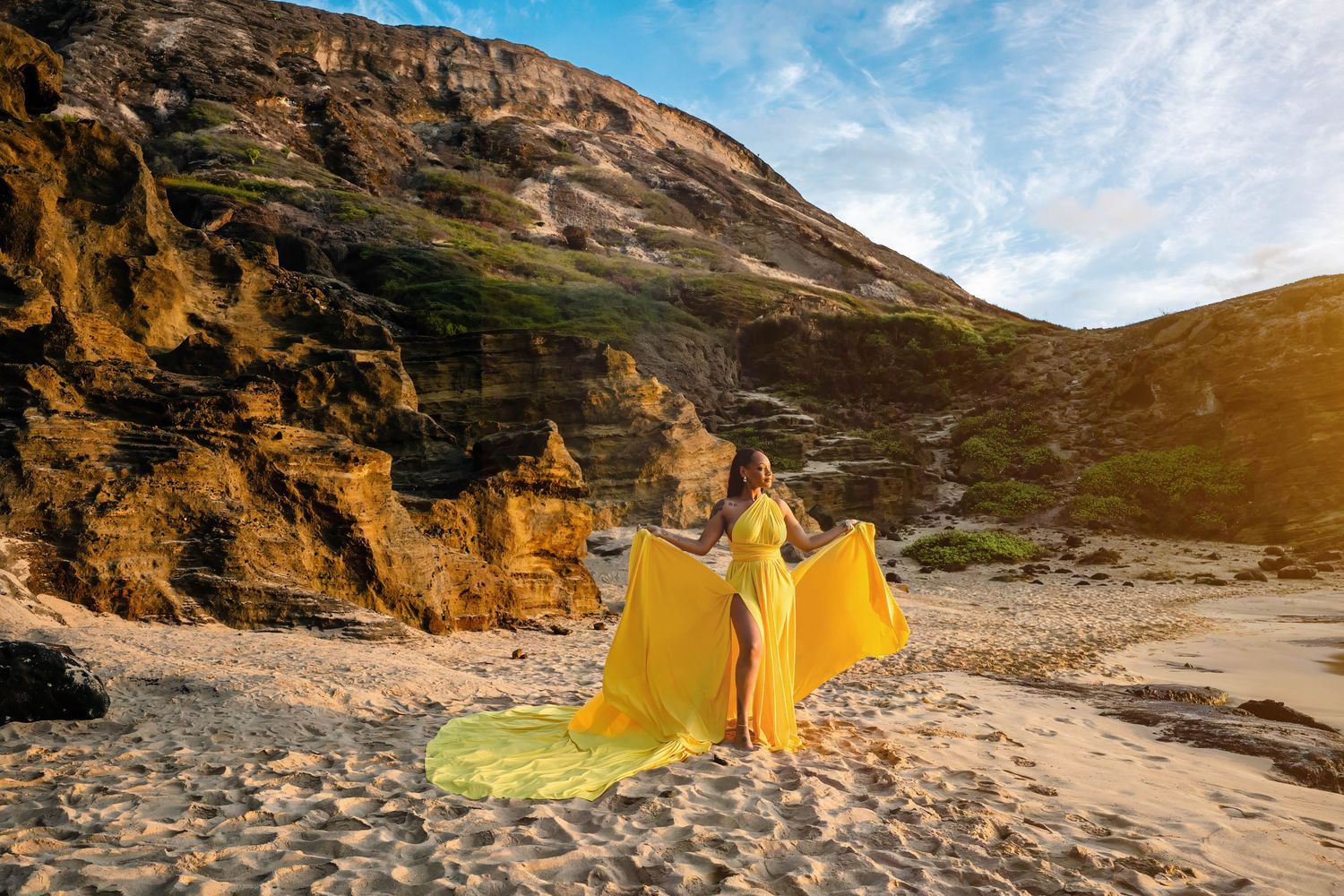 A scenic beach cove with dramatic cliffs and yellow tent installations against a rugged coastal landscape at sunset.