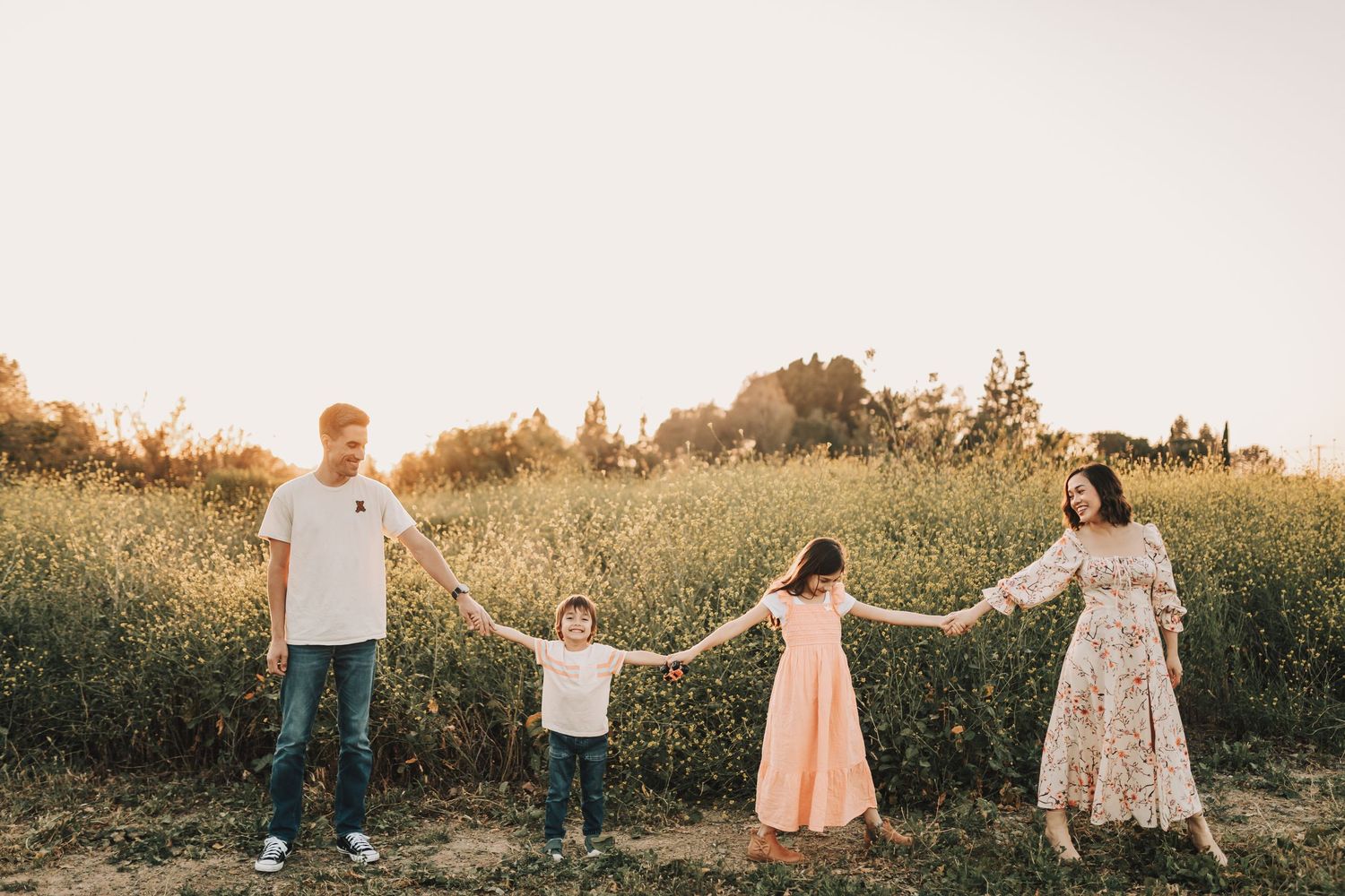 A group of people dance and play in a sunlit meadow during golden hour, creating joyful silhouettes against the setting sun.
