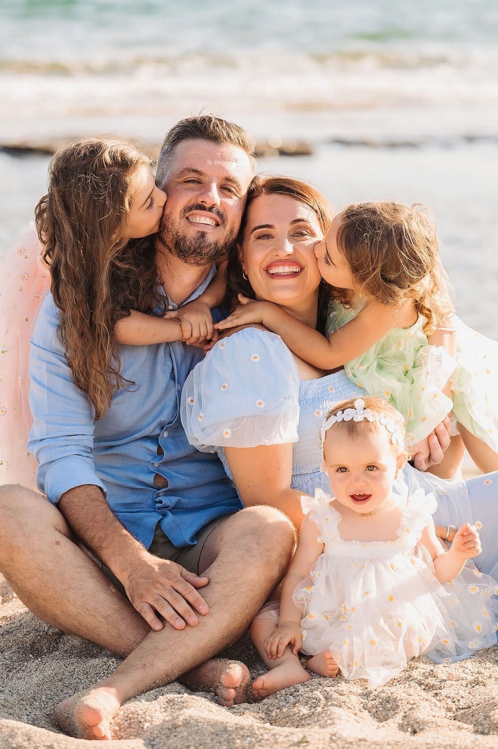 Happy family moment captured during sunset at the beach with everyone sitting in the sand.