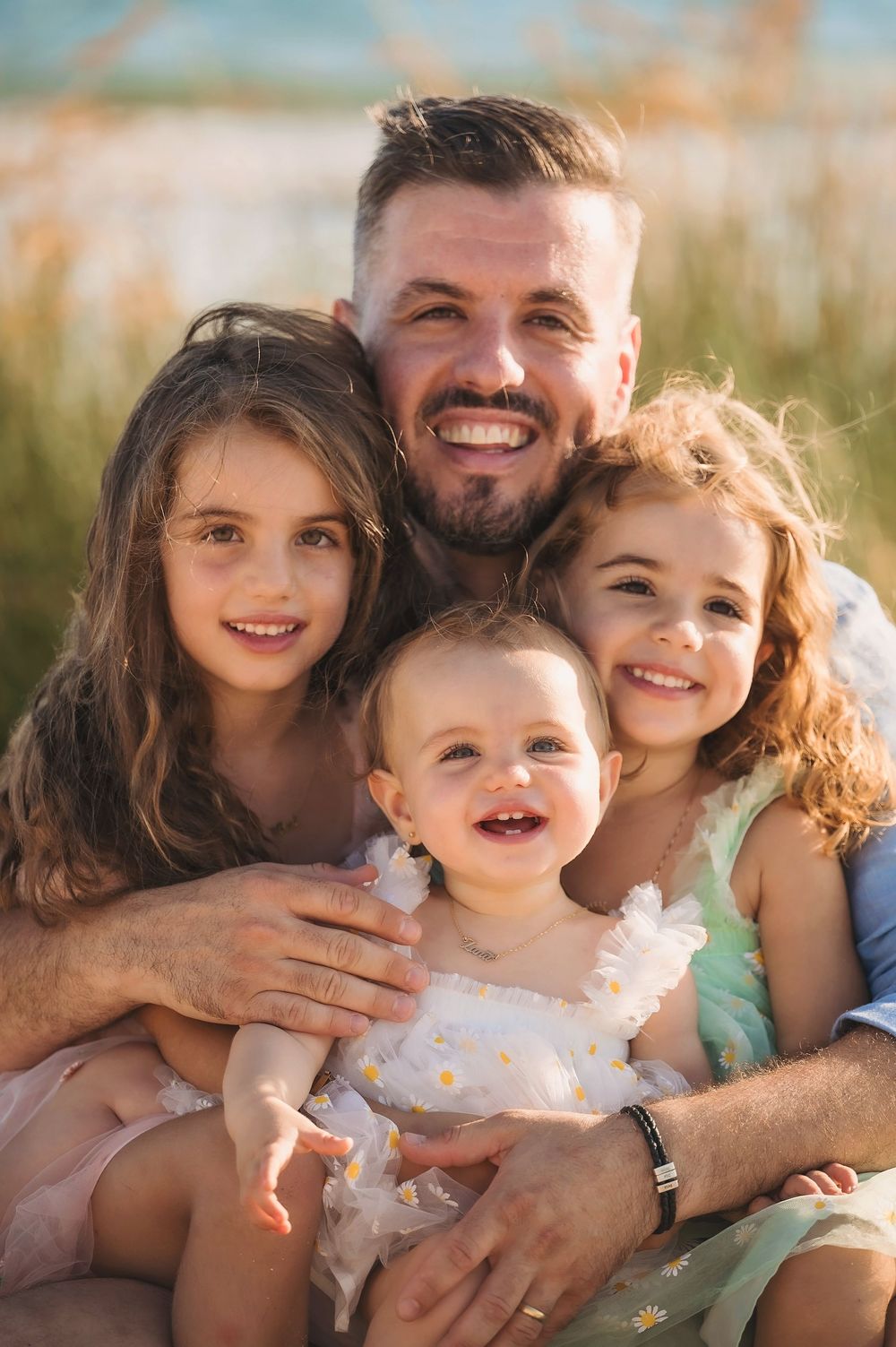 A loving family enjoys playful candid moments together during a beach photoshoot in warm golden light.