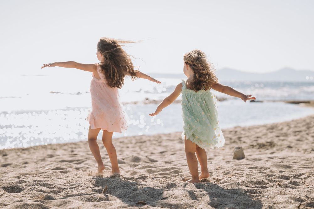 Two children dancing carefree on a sunny beach with arms outstretched like wings.