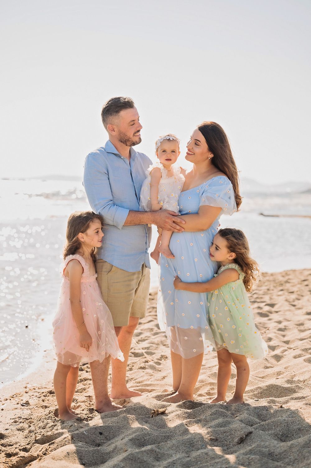 A family of five in coordinating pastel outfits enjoys a sunny day together at the beach.