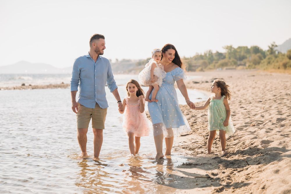 A family walking along the shoreline of a sandy beach with gentle waves rolling in on a bright day.