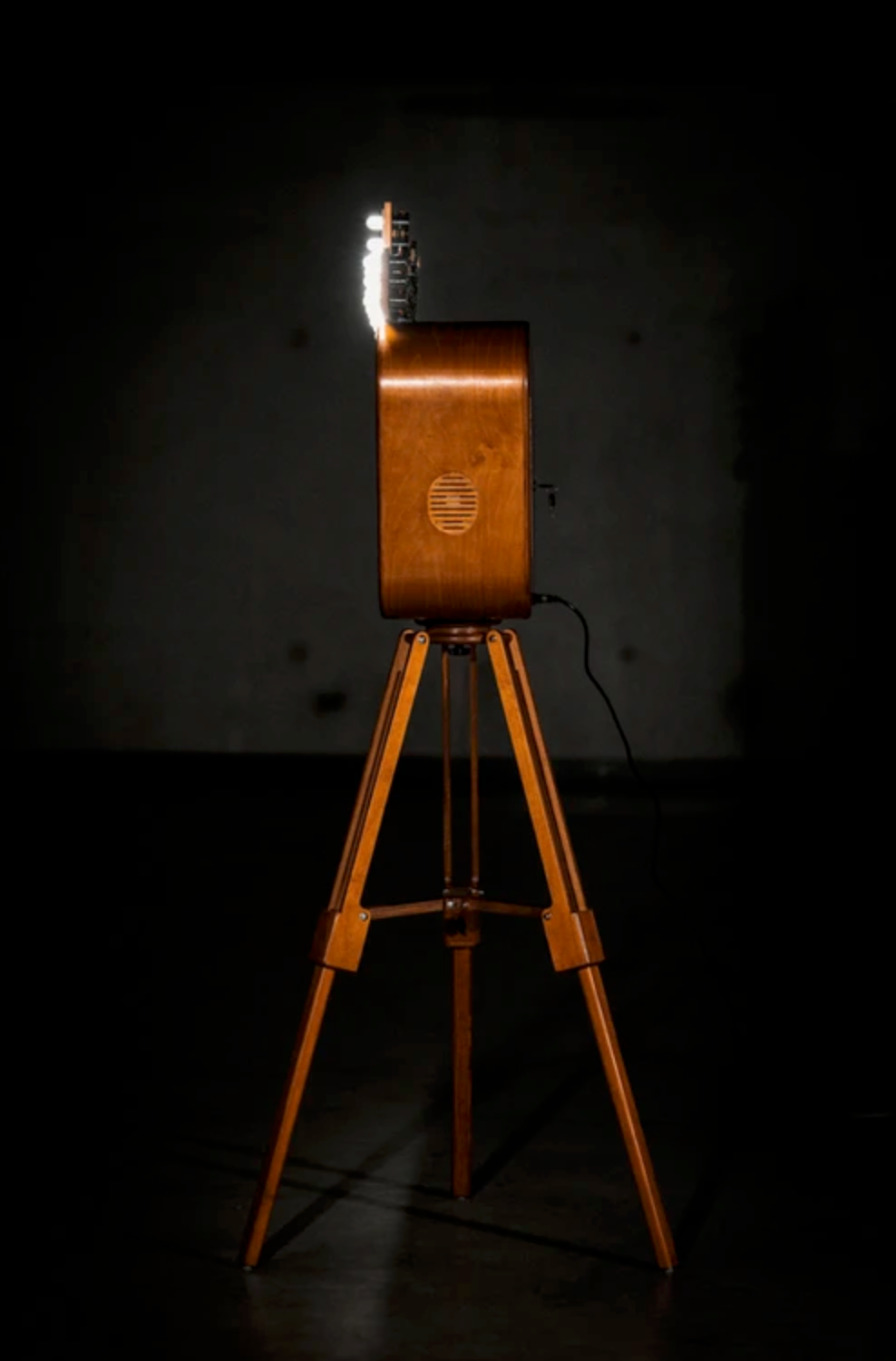 Vintage wooden camera on classic tripod stand photographed against dark background showcasing historic photography equipment.
