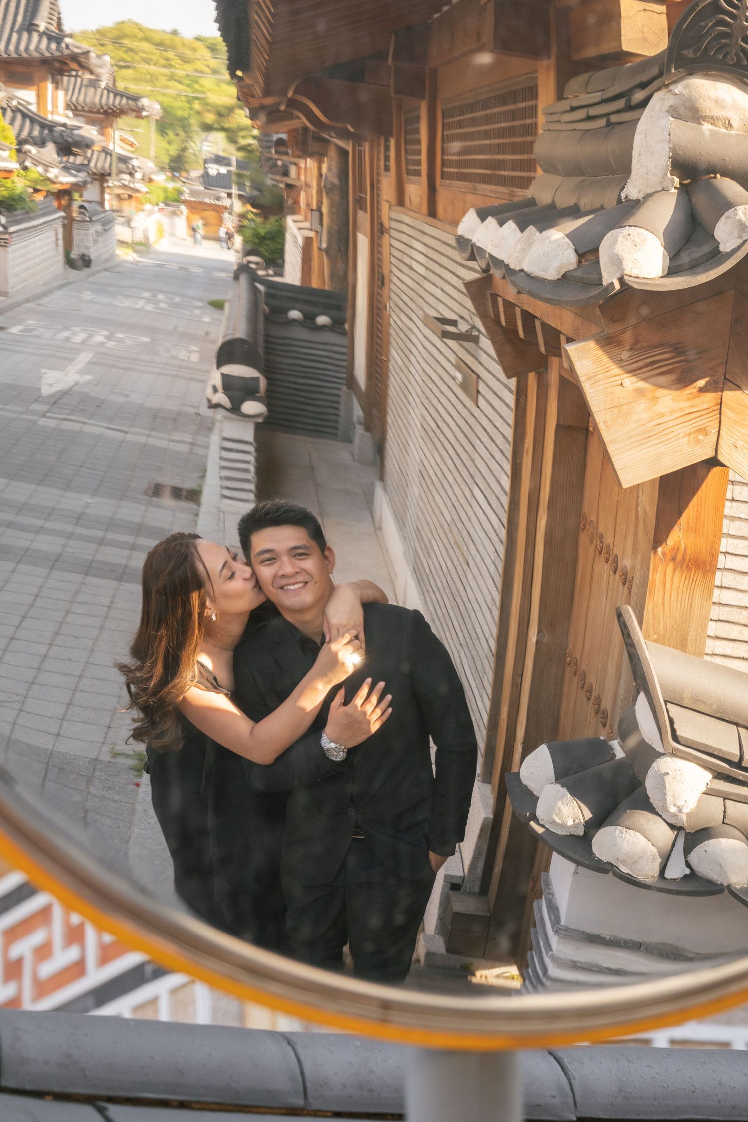 Romantic couple shares tender moments reflected in traditional Asian architectural mirror panels along a historic walkway.