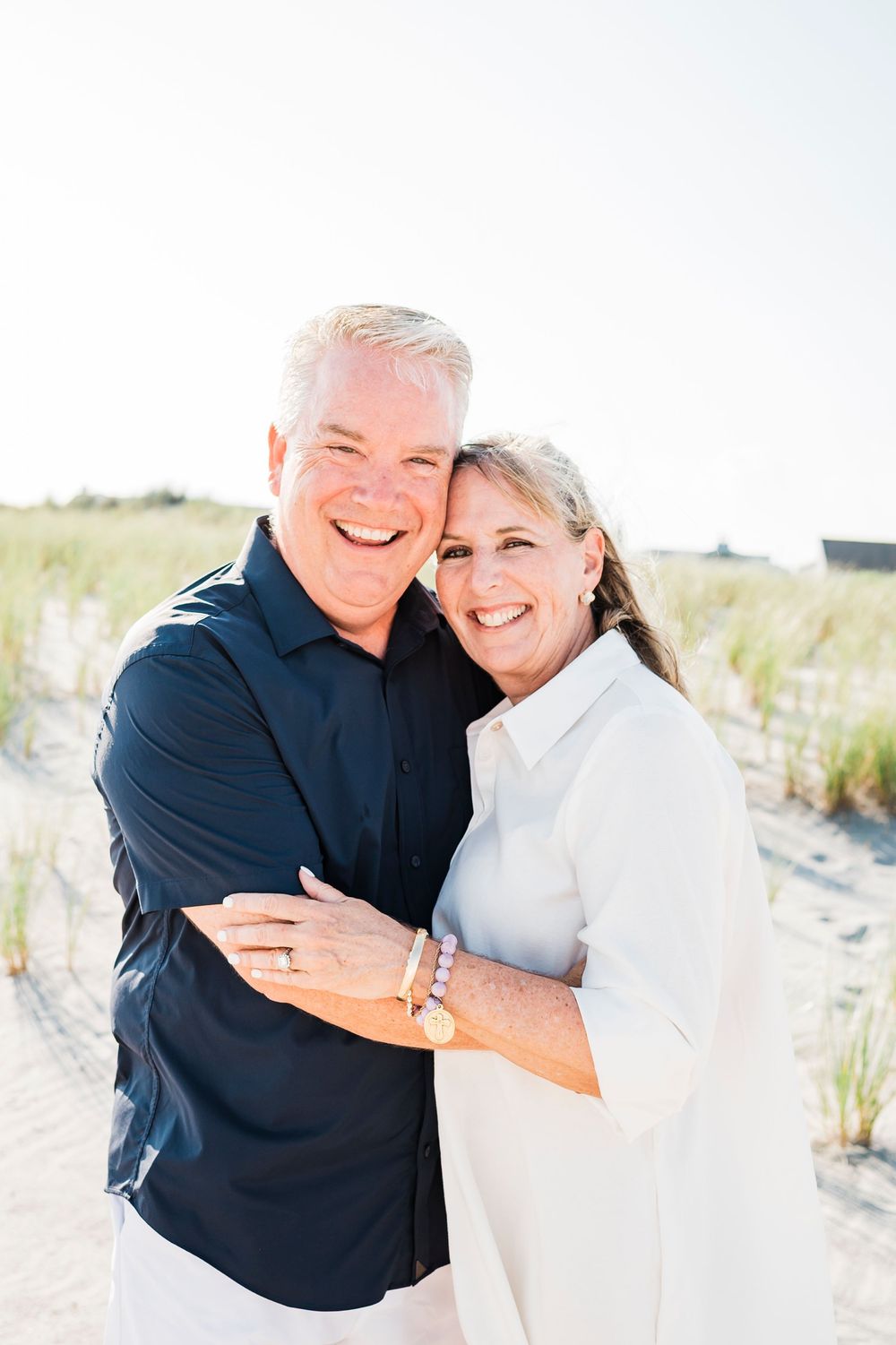 Couple embracing and laughing together on a bright sandy beach.