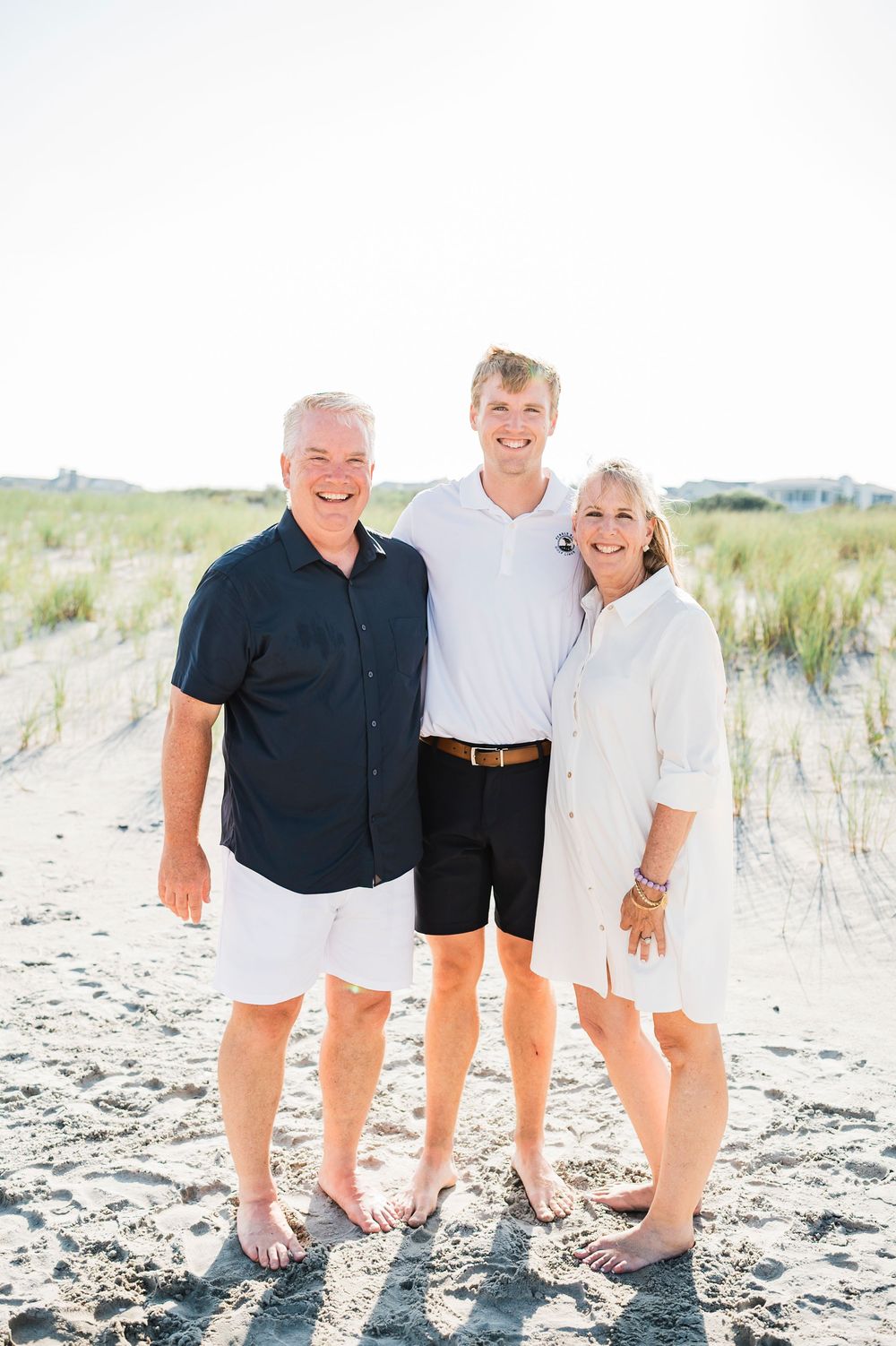 People wearing navy and white outfits gather for a casual photo session on a sandy beach with dunes.