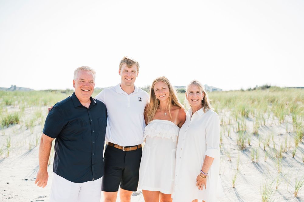 A group poses in coordinated navy and white clothing against a coastal sand dune landscape.