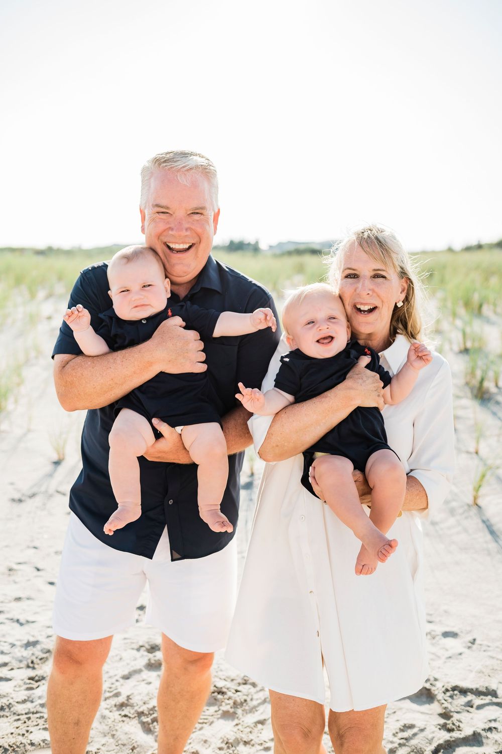 Cheerful group moment captured on a beach with everyone dressed in coordinating navy and white outfits.