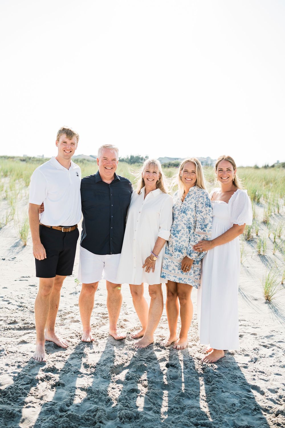 Group portrait of family members standing together on a sandy beach wearing coordinated summer attire.