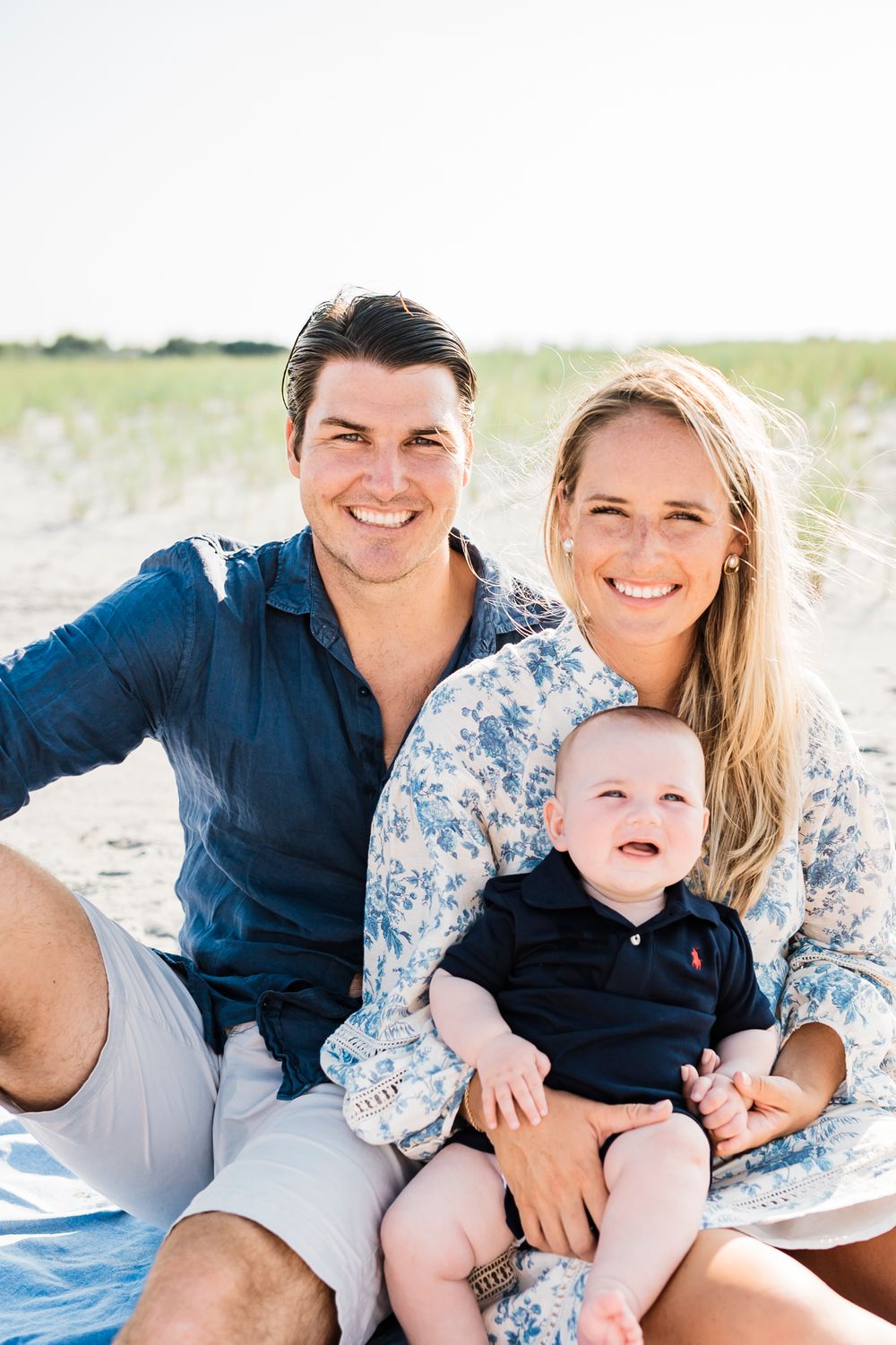 Happy family relaxes together on blanket during casual beach photoshoot.