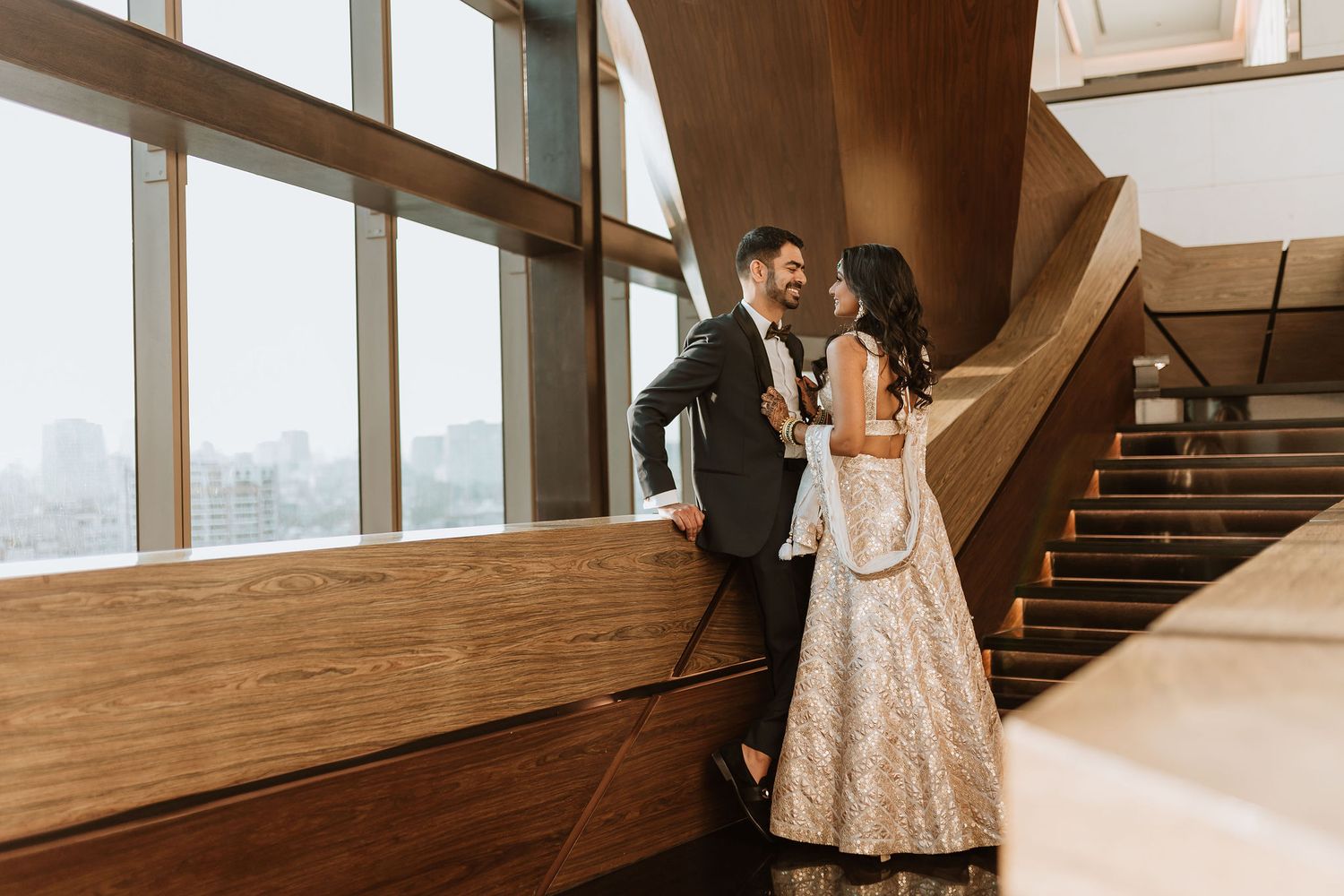Elegant wedding couple poses in a modern architectural space with dramatic lighting and staircase.