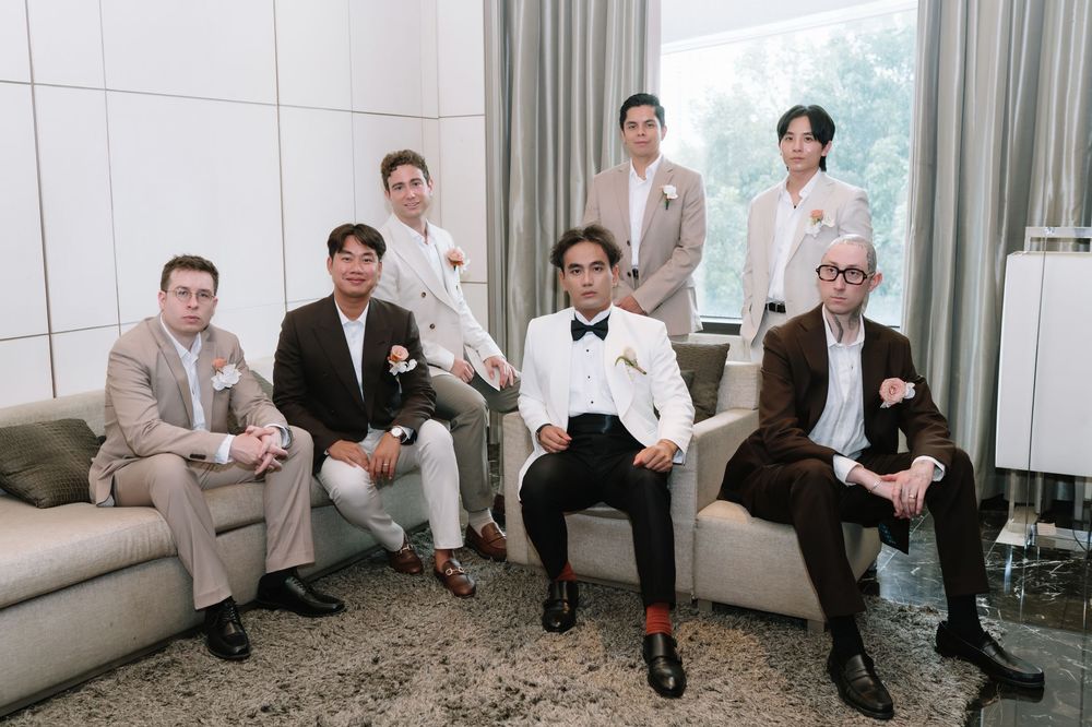Group of groomsmen in elegant suits posing together in a bright modern hotel suite.