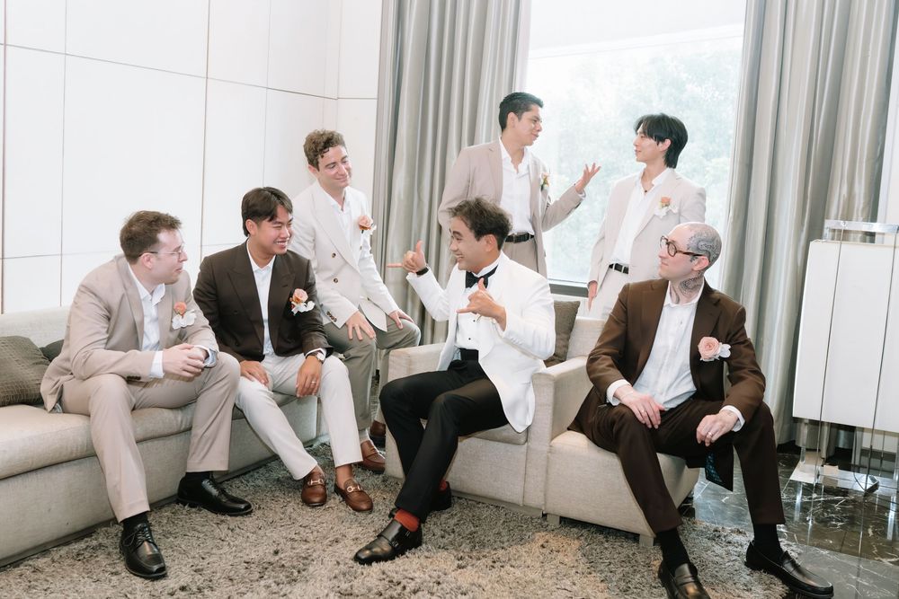 Group of groomsmen in suits laughing and relaxing together in an elegant hotel suite before a wedding.