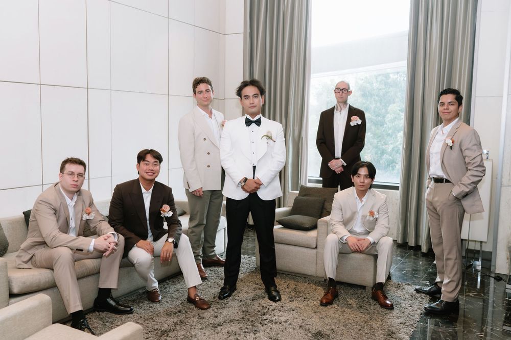 Groom in white tuxedo poses with groomsmen in neutral suits in a bright luxury hotel suite.