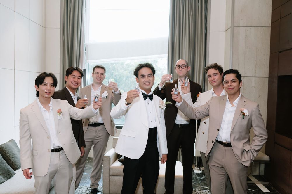 Groom and groomsmen in suits raising champagne glasses in a toast before a wedding celebration.