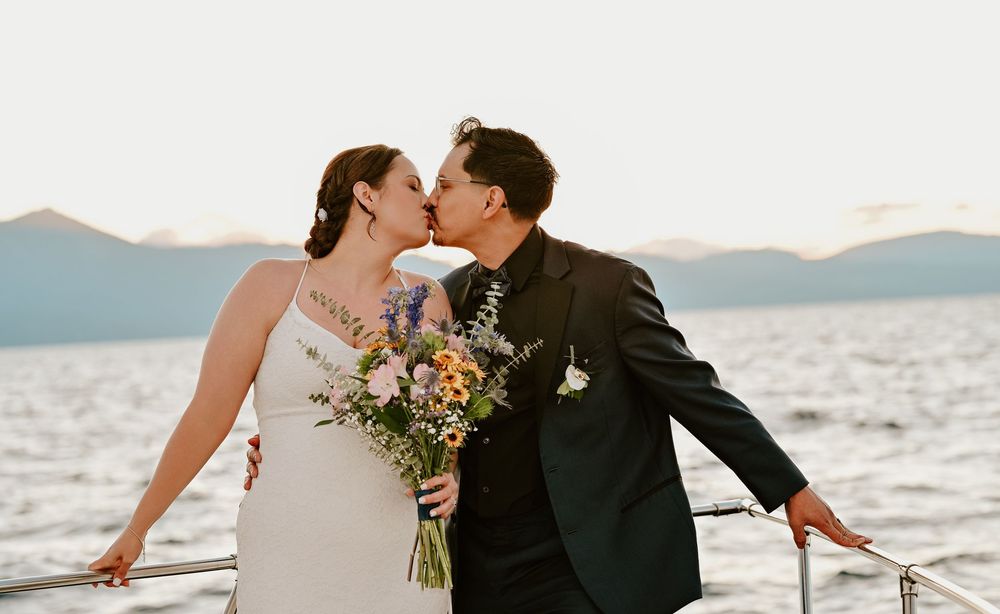 Romantic couple sharing an intimate moment on a boat during sunset by the ocean with mountains in the background.