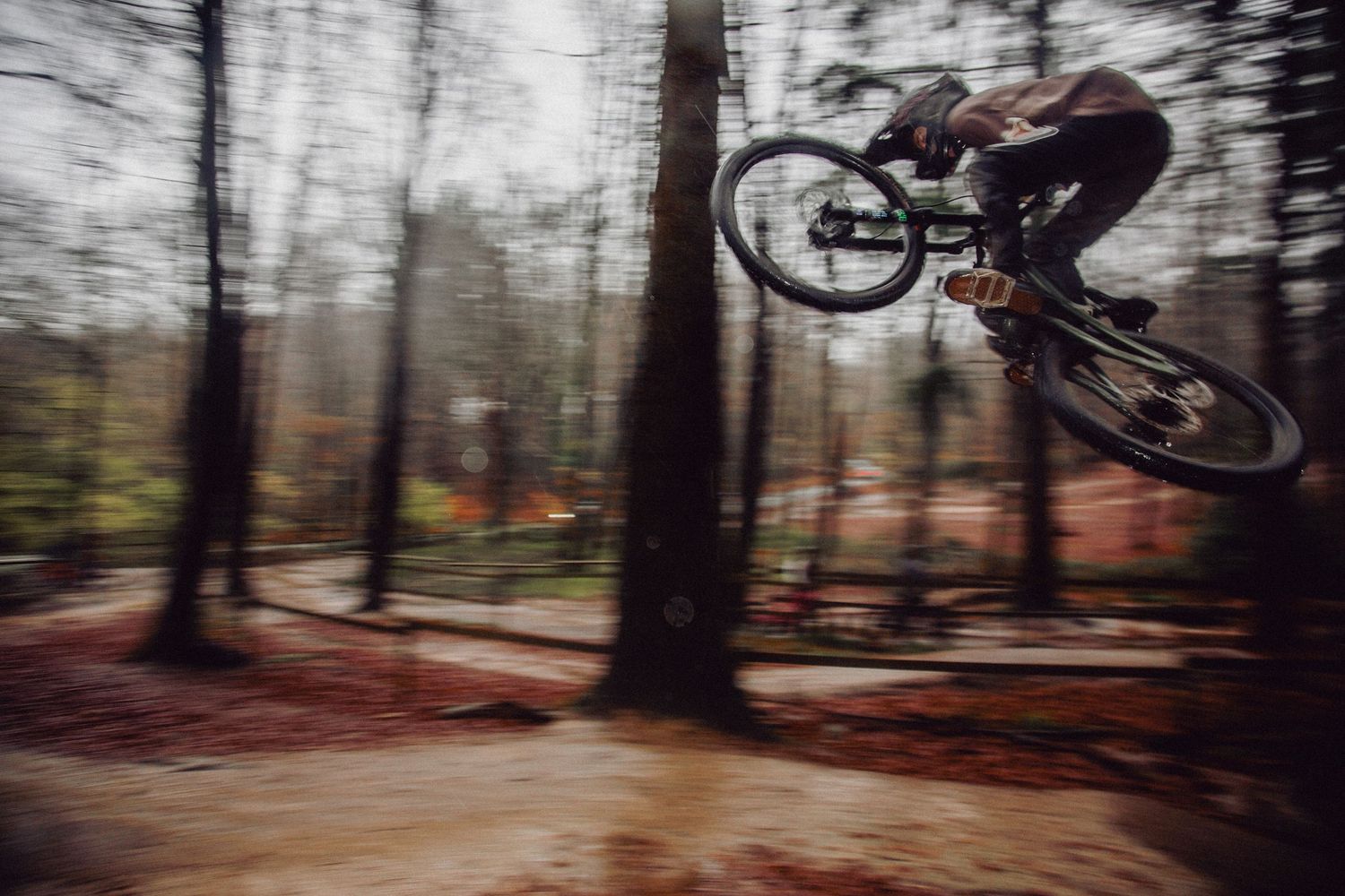Mountain biker performs aerial jump in blurred forest setting during action sports photography.
