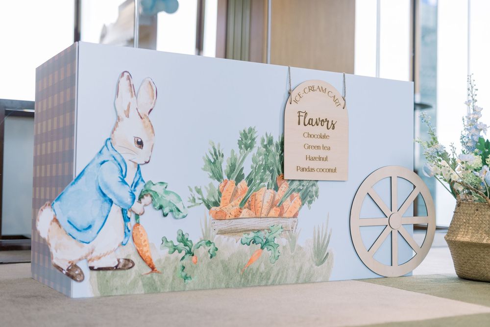 A Peter Rabbit themed party backdrop featuring a painted illustration of the character with carrots and a cart.