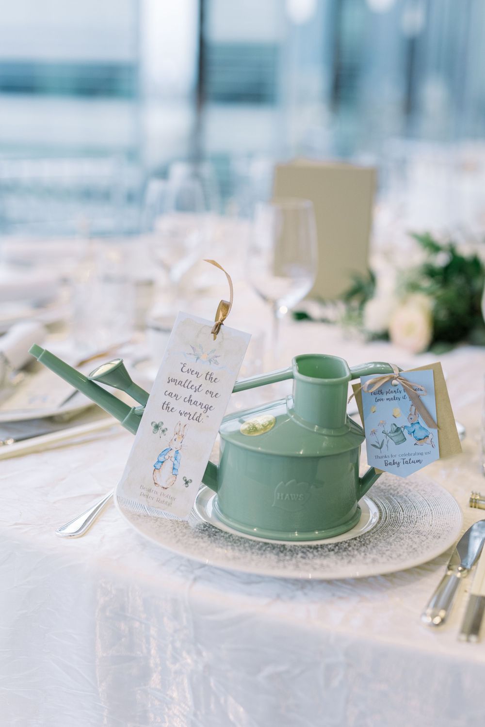 Elegant place setting with mint green teacup and saucer adorned with delicate place card on white tablecloth.