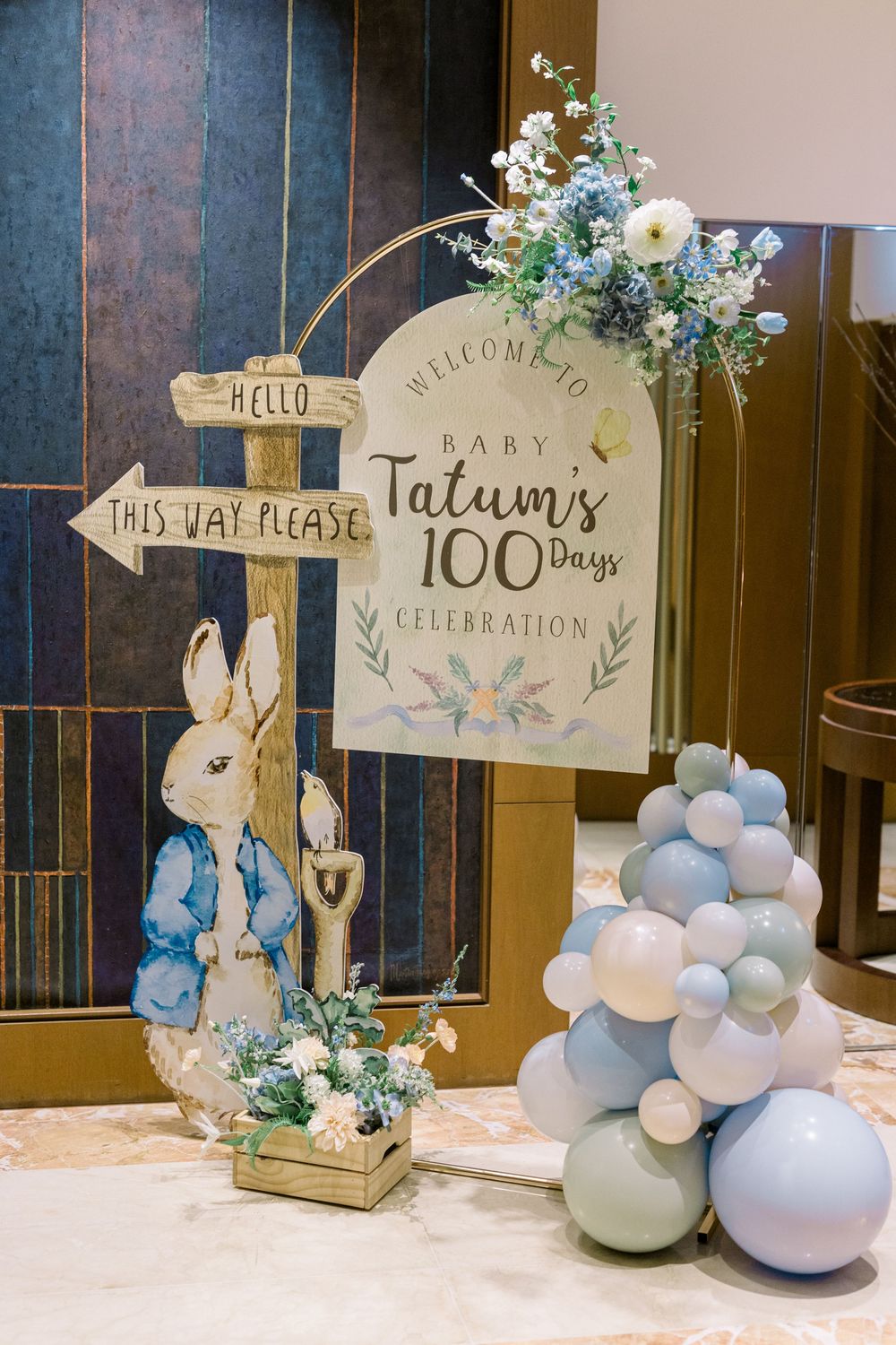 Peter Rabbit themed 100 days celebration display with balloon arch, welcome sign and directional post in blue and white decor.