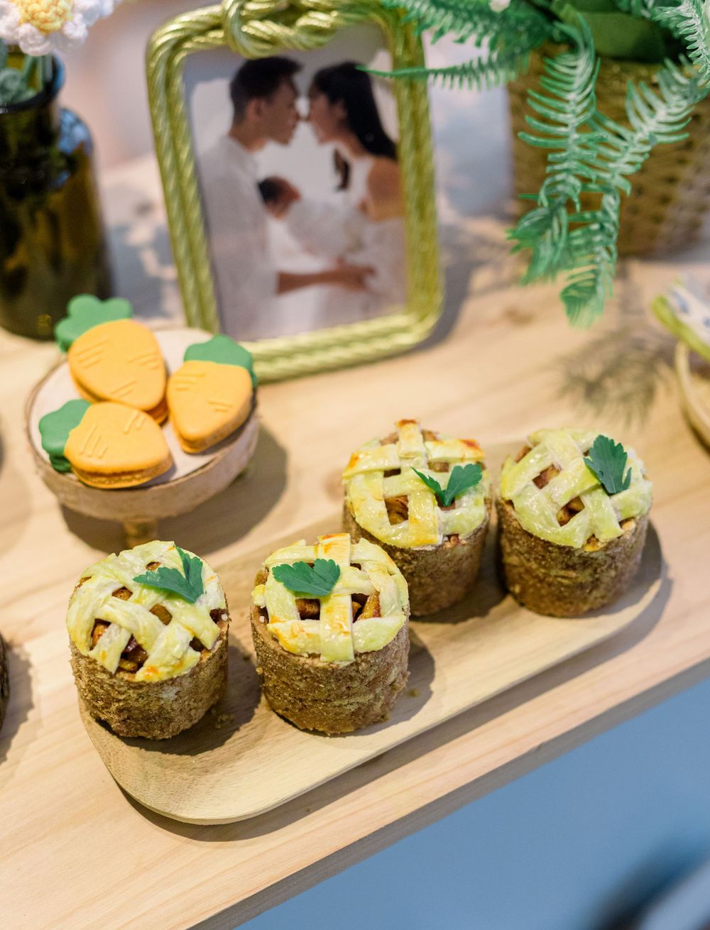 Mini green sandwich-style macarons with herbal filling arranged on a wooden serving platter with tropical fern decor.