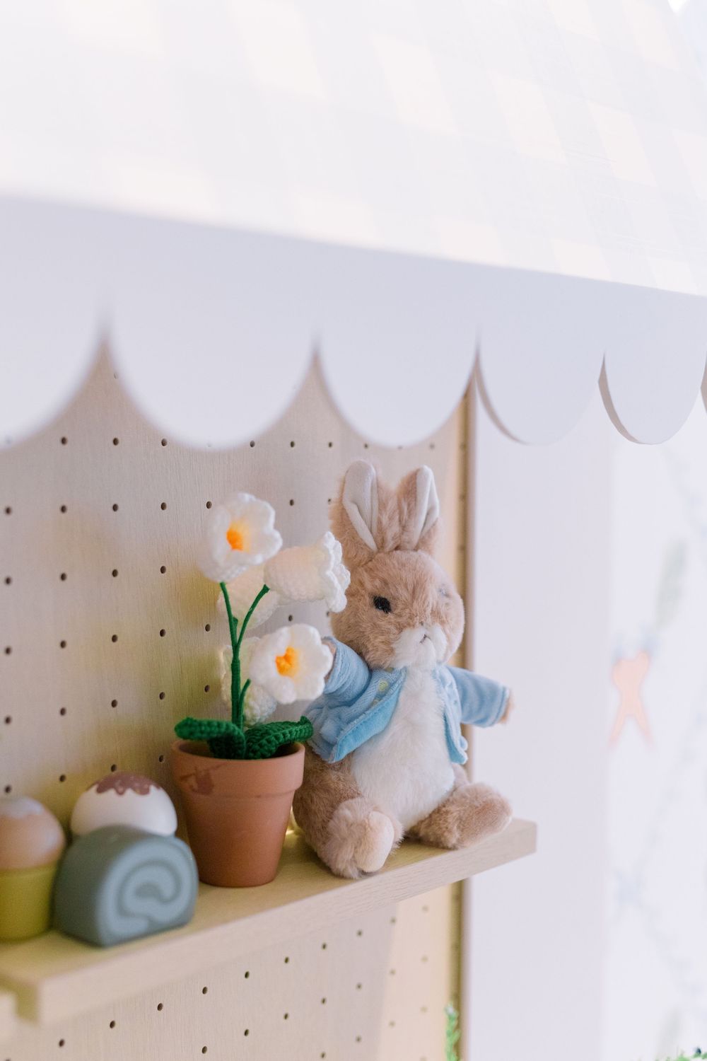 Small ceramic pots with artificial flowers and stuffed bunny decorations displayed on white pegboard shelves.
