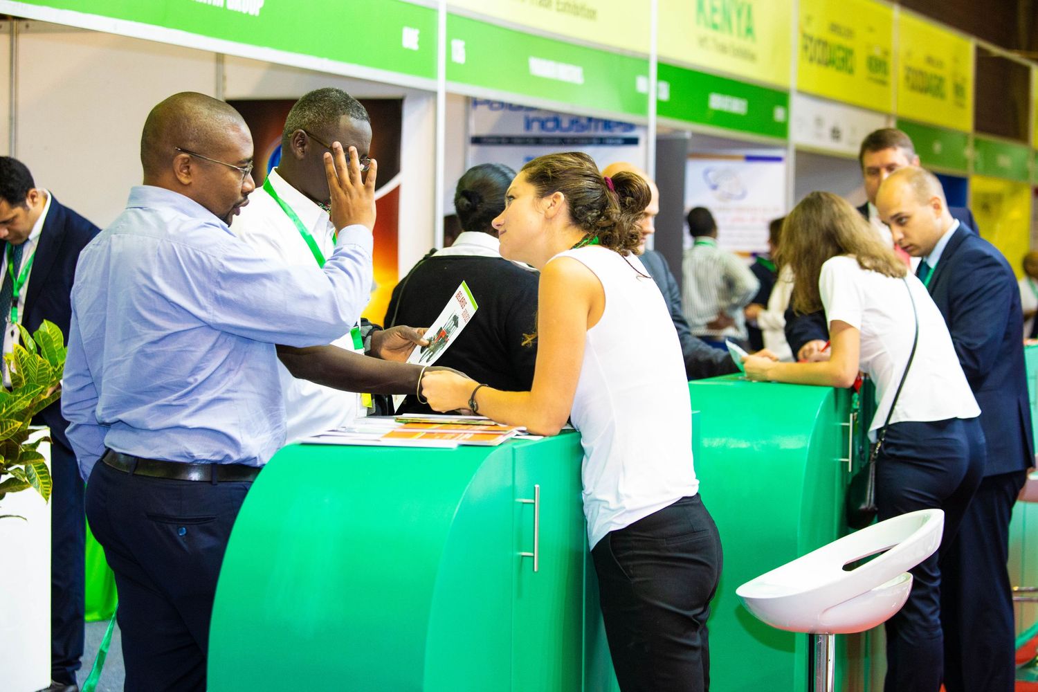 Business professionals gather around a trade show booth display examining products at an industry exhibition.