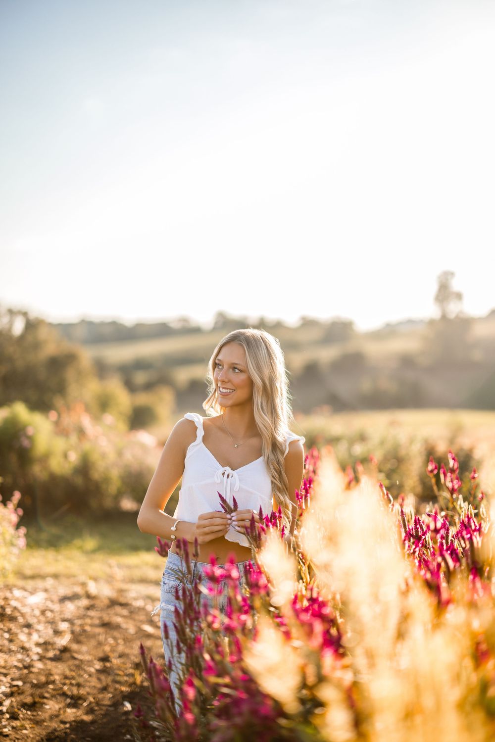 A dreamy golden hour photoshoot in a field of pink wildflowers with warm sunlight creating a magical atmosphere.