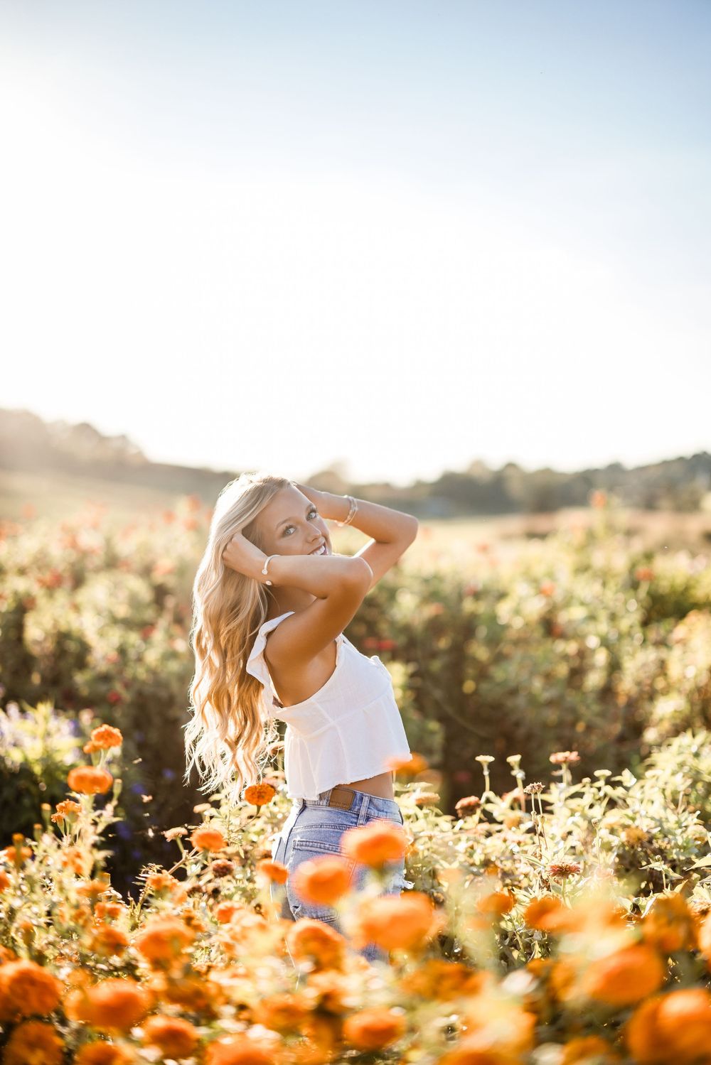 Person in white dress twirling joyfully among orange wildflowers at golden sunset in a meadow.
