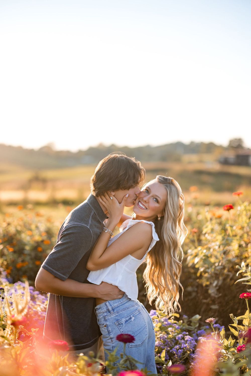 A romantic couple embraces in a sunlit flower field during golden hour sunset.