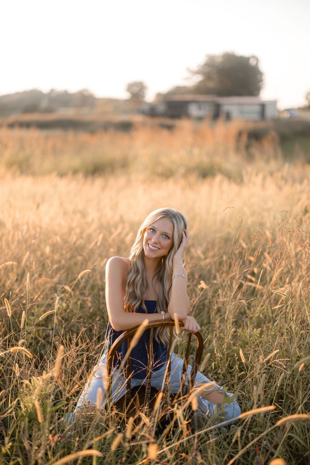 Person relaxing in tall golden grass during sunset with mountains in background.