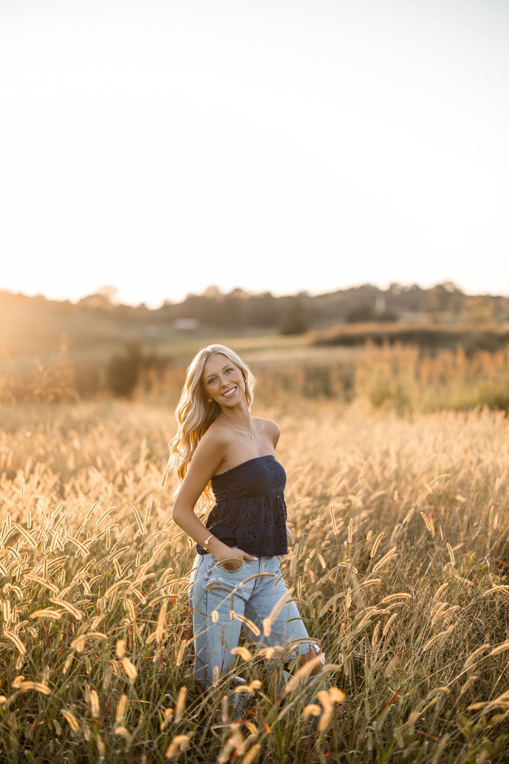 A figure sits in a golden wheat field at sunset wearing jeans and a dark top.