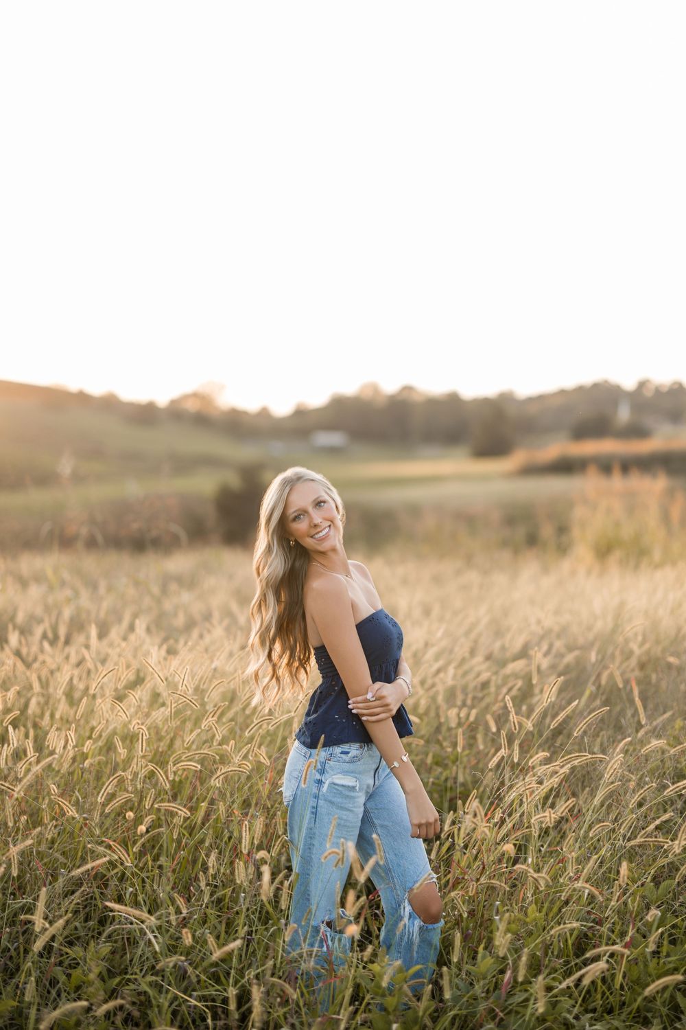 Person in ripped jeans and dark top poses in a golden wheat field at sunset creating a dreamy summer scene.