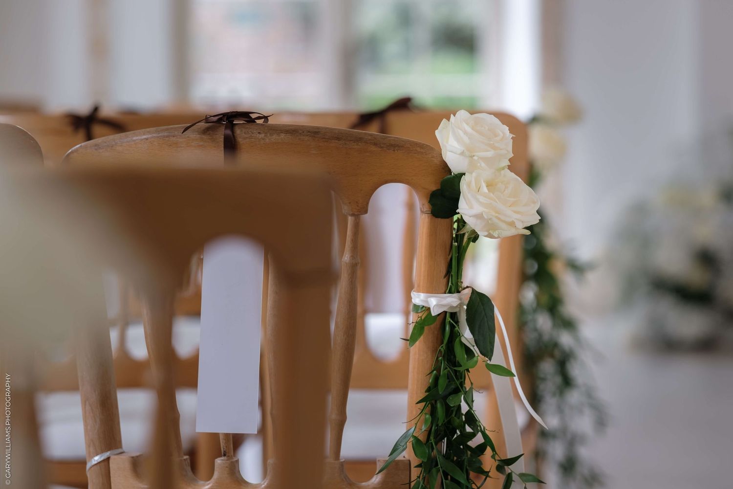 White floral arrangements and candles decorate an elegant indoor wedding venue with soft lighting and white chairs.