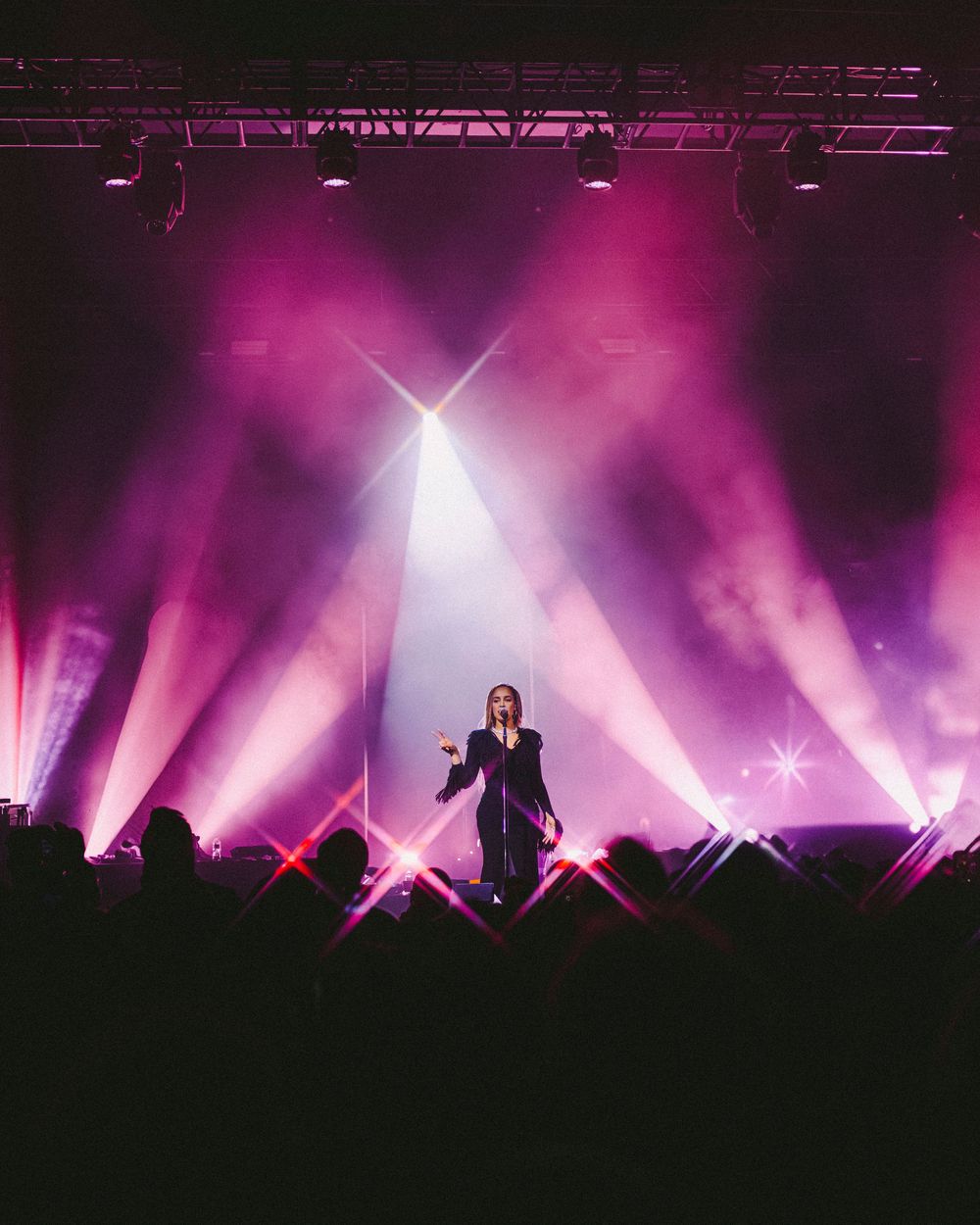 Concert stage illuminated with vibrant purple lights and fog creating a dramatic silhouette effect during performance.
