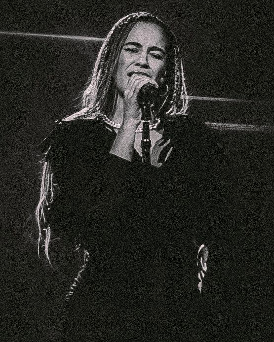 Black and white photo of a performer singing emotionally into a microphone during a concert performance.