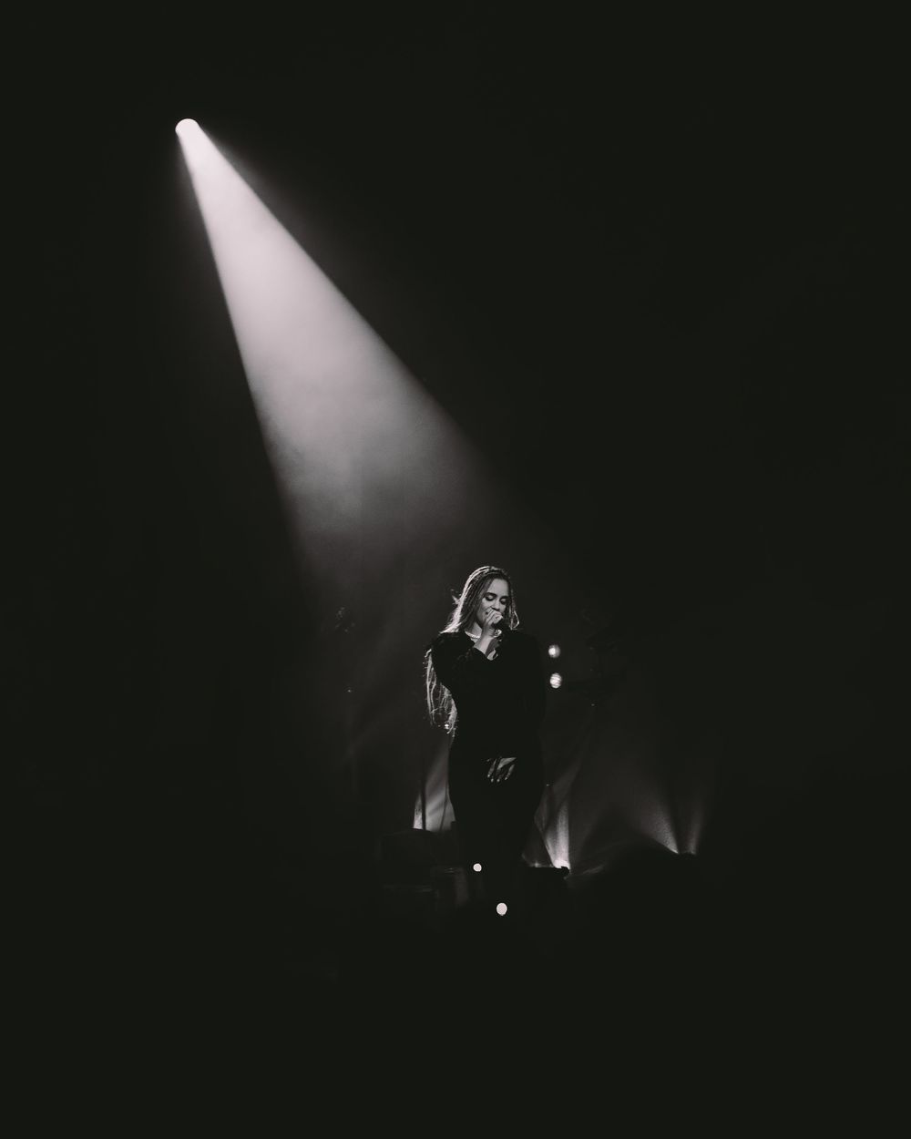 A dramatic black and white stage performance with a single spotlight beam illuminating a performer in the darkness.
