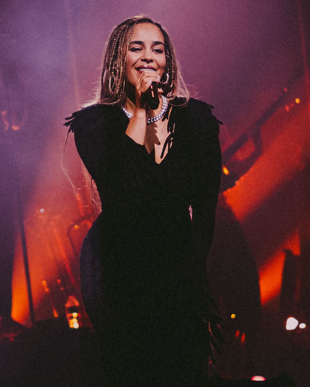 A performer sings on stage in a black outfit against a dramatic purple and red-lit backdrop during a concert performance.