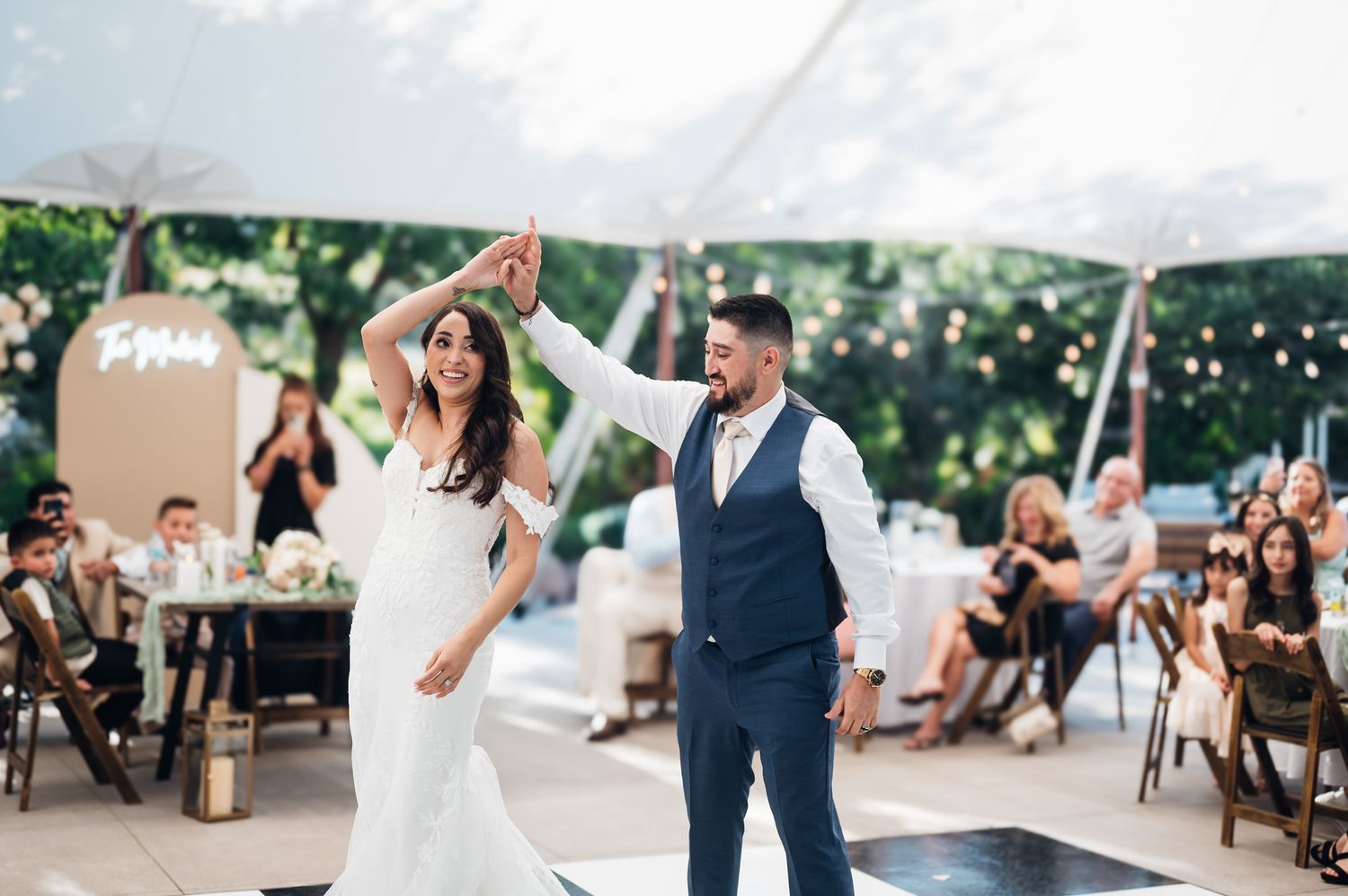 A couple shares an intimate dance beneath a large outdoor tent at a romantic wedding reception.